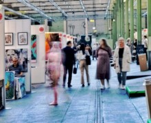 Während der Art Nordic wurden auch Inszenierungen gezeigt. Hier sieht man die Frau im gestrickten Outfit unscharf in der Bewegung, und die Besucher, die den Gang entlang laufen.